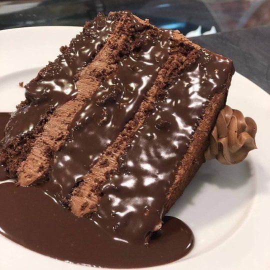 Slice of chocolate layer cake with shiny chocolate glaze on a white plate