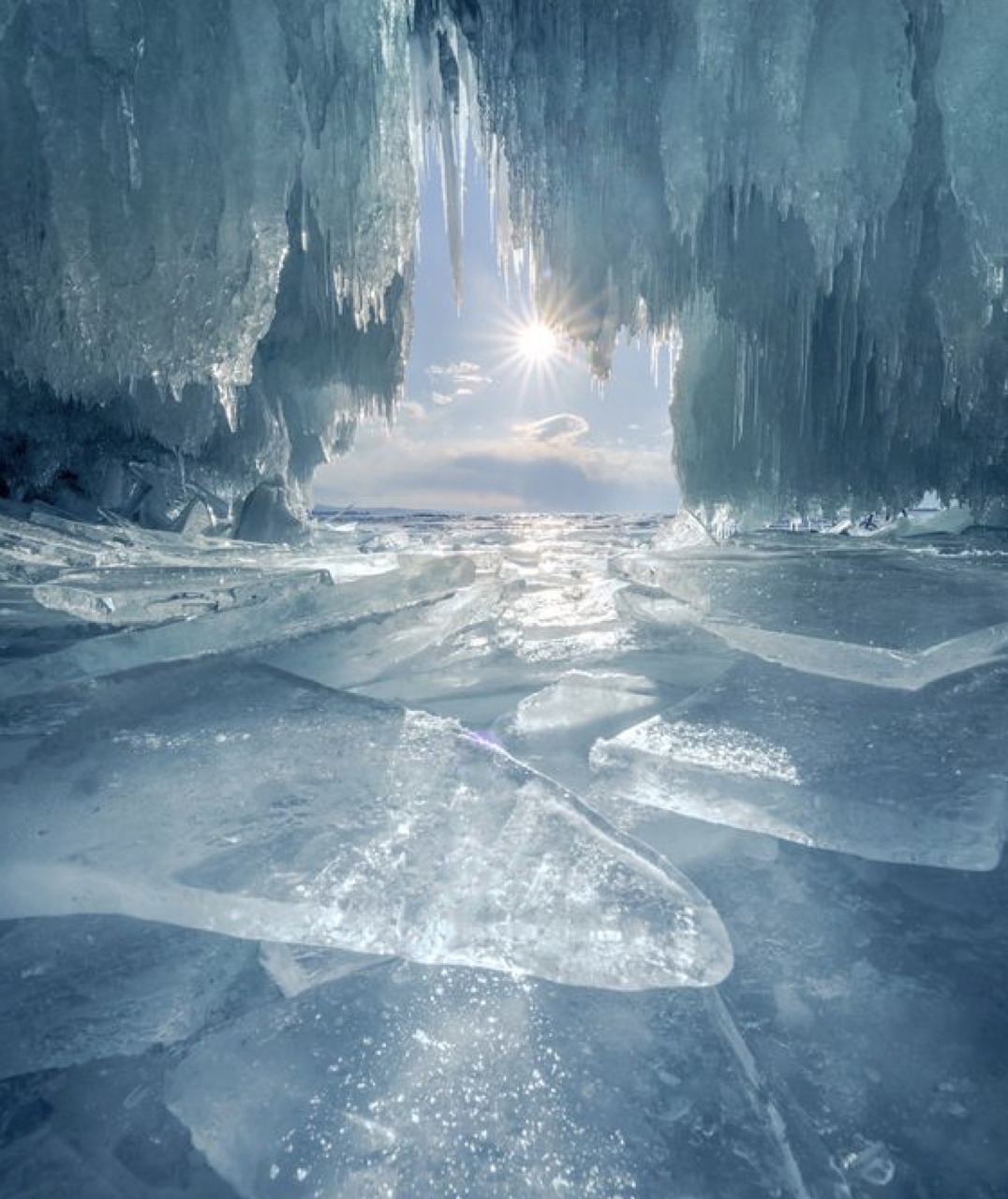 Sunlight inside a blue ice cave above cracked frozen water in Antarctica
