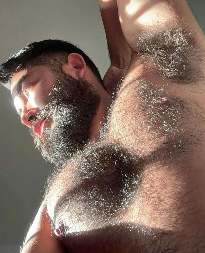 Close-up of a muscular bearded man raising his arm showing hairy chest and armpit