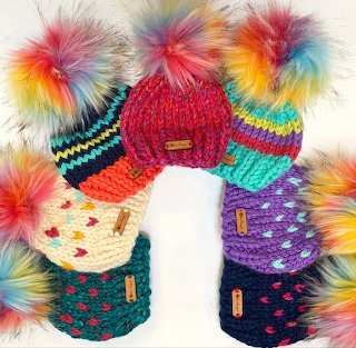 Colorful knitted beanies with fluffy pom-poms arranged in a circle on a white background