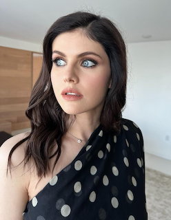 Alexandra Daddario wearing a black one-shoulder polka dot dress indoors