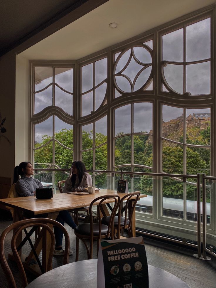 Two people at a café table by large arched windows with a view of Edinburgh's green hillside