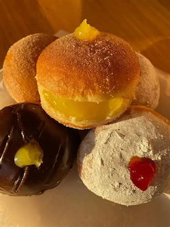 Assorted pastries: cream bun, chocolate donut, powdered cookie, and glazed rolls arranged together