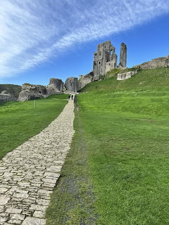 Stone path leading uphill to ruined Corfe Castle surrounded by green grass under blue sky