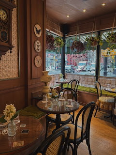 Cozy cafe interior with wooden walls, round tables, chairs, flowers, and large street-facing windows