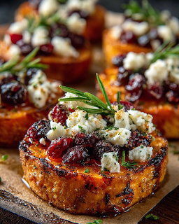 Roasted sweet potato rounds topped with goat cheese, cranberries, and rosemary on a wooden surface