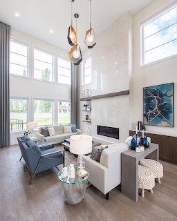 Contemporary double-height living room with white sofas, blue chairs, pendant lights, and a modern fireplace