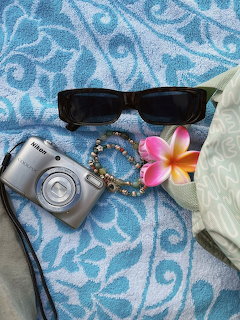 Beach accessories including sunglasses, camera, bracelet and tropical flower on blue towel