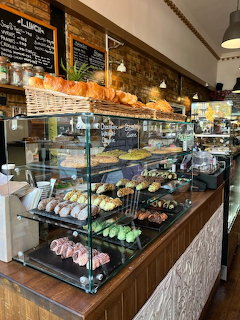 Cafe bakery glass display case filled with assorted pastries, croissants, and desserts with brick wall behind