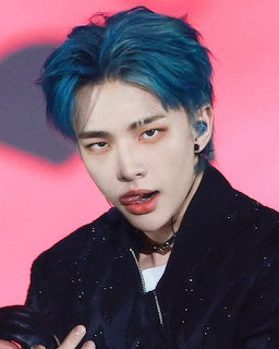 Young man with blue hair and red lips wearing a black outfit against a pink-red background