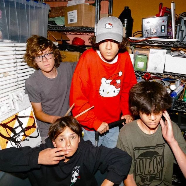 Four teenage boys posing in a cluttered storage room with shelves and boxes