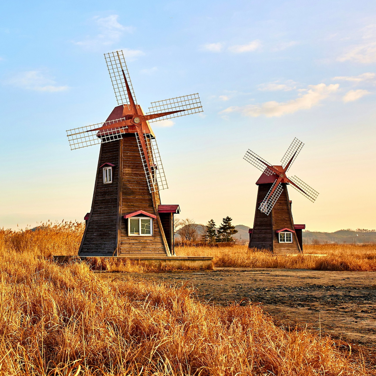 Two wooden windmills in a dry field beneath a blue evening sky