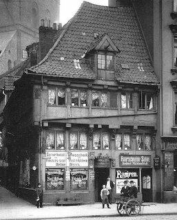 Black and white photo of historic half-timbered building with steep roof and storefronts