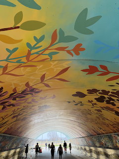 People walking through tunnel with colorful floral mural on curved ceiling