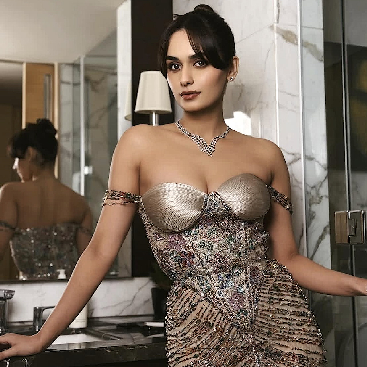 Woman in an embellished strapless gown posing indoors with mirrors behind her