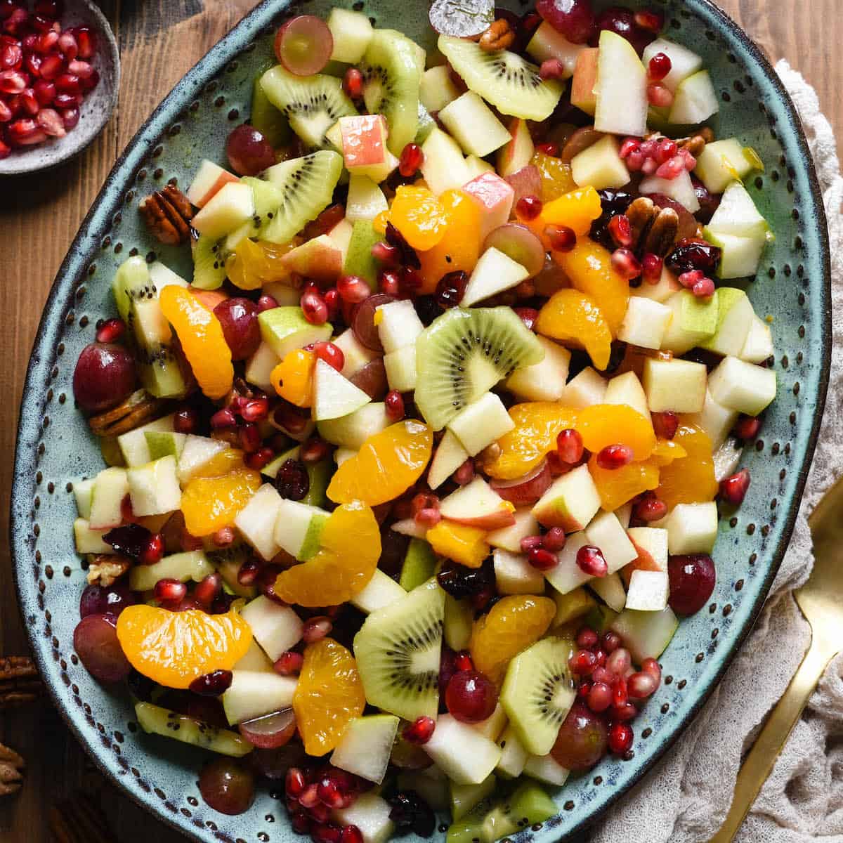 Colorful fruit salad with kiwi, orange, apple, grapes, and pomegranate on blue platter