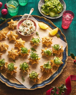 Round platter of golden fried appetizers topped with lettuce, surrounded by colorful drinks and garnishes on teal background