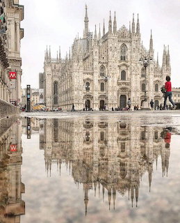 Milan Cathedral reflected in a rain puddle in a city square