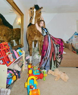 Woman in vibrant flowing outfit standing with taxidermy giraffe in toy-filled room