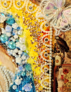 Close-up of mixed media art with rhinestones, pearl beads, blue flowers, and a vintage bird illustration