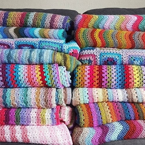 Stacks of colorful crocheted blankets with striped patterns and textured stitches