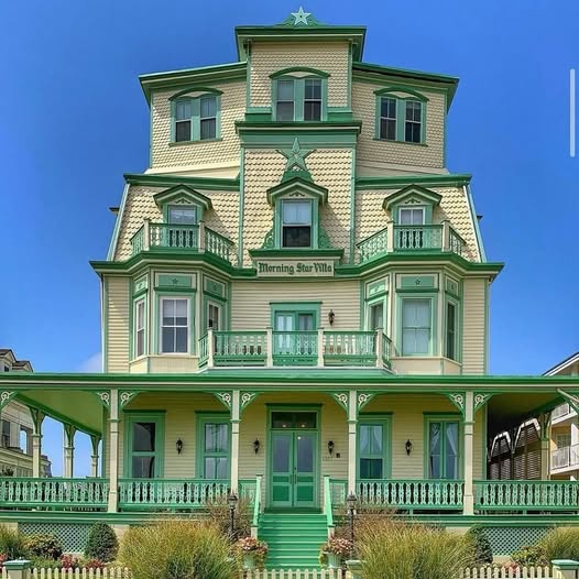 Victorian-style house exterior with green trim, porches, and bay windows against a blue sky