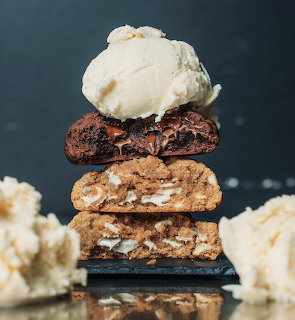 Vanilla ice cream on a stacked brownie and cookie dessert with crumbs in the foreground.