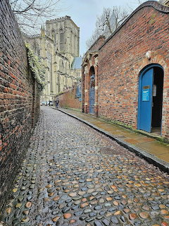 Narrow cobblestone alley between brick walls leading to a cathedral tower in York