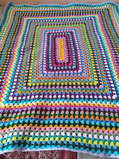 Colorful handmade crochet blanket with rainbow granny square pattern laid on wooden floor