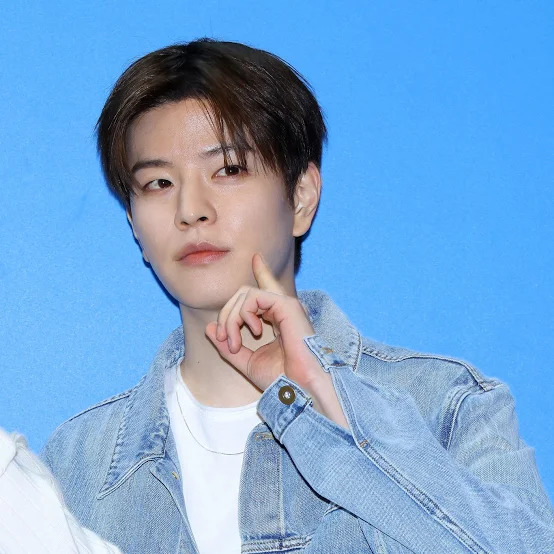 Young man in a denim jacket posing against a bright blue background