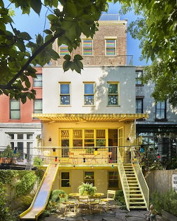 Yellow townhouse with balcony, stairs, and a small backyard patio between city row houses