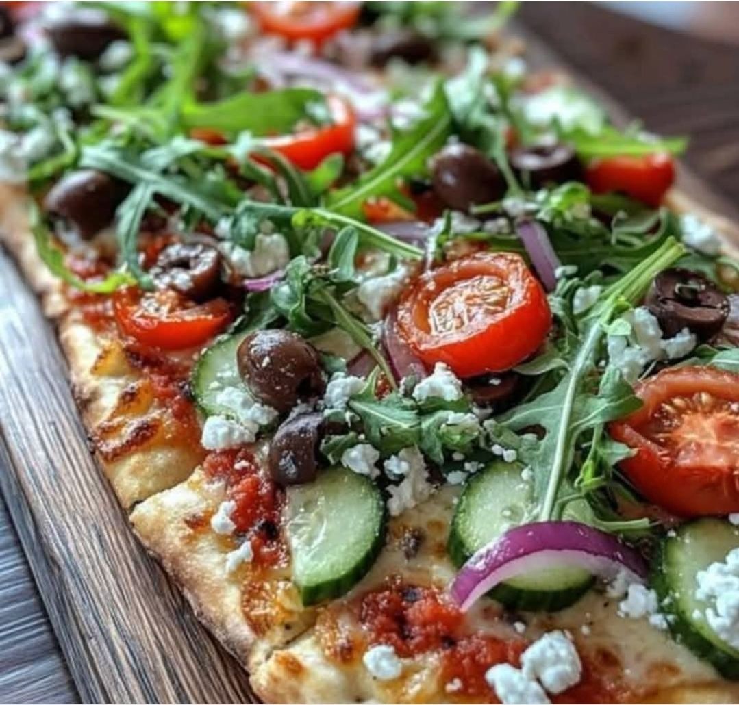 Close-up of a vegetable flatbread pizza with tomatoes, cucumber, olives, onion, arugula, and cheese