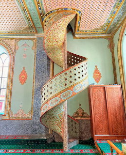 Ornate spiral staircase with gold details in colorful mosque interior with decorative Islamic patterns
