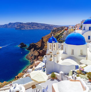 White buildings with blue domes on a Santorini cliff above the sea