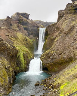 Tall waterfall plunging between steep mosy cliffs into a turquoise pool in Iceland