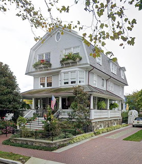 White gambrel-style house with porch and garden in residential neighborhood