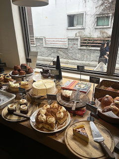 Cafe counter displaying assorted cakes, pastries, and baked goods near a window
