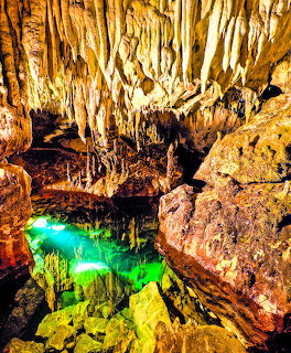 Interior of Dragon Cave in Kastoria with stalactites hanging from ceiling and glowing green underground pool