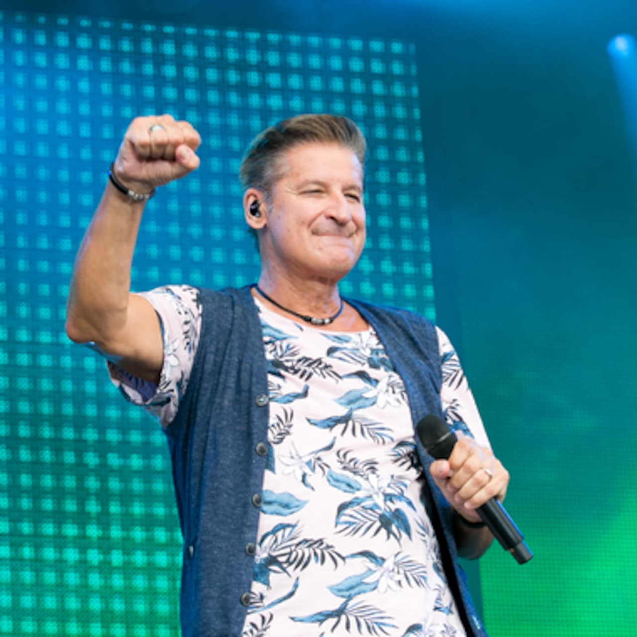 Male singer on stage with raised fist holding microphone under blue and green lights