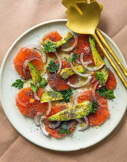 Overhead view of citrus salad with grapefruit, avocado, onion and herbs on white plate