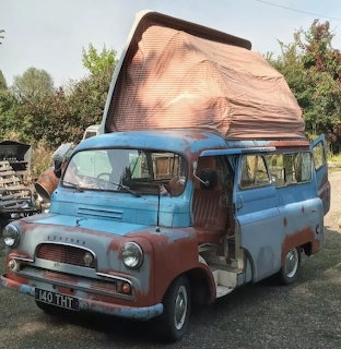 Vintage blue and red Bedford CA Dormobile camper van with raised canvas roof parked on grass