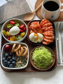 Korean breakfast tray with sausage, eggs, fruit salad, blueberries, cabage, and coffee on wooden table