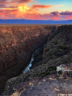 Rio Grande Gorge canyon with river below steep rocky cliffs and colorful sunset clouds above
