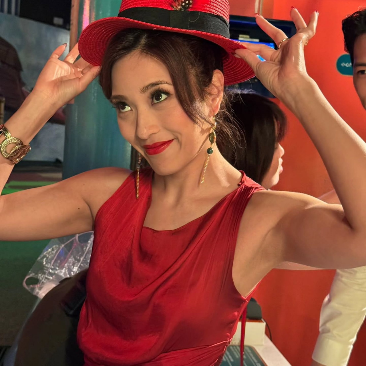 Woman in red dress and decorative red hat smiling at camera with arms raised