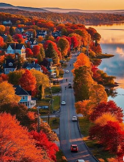 Aerial view of a tree-lined road through a colorful autumn lakeside town at sunset