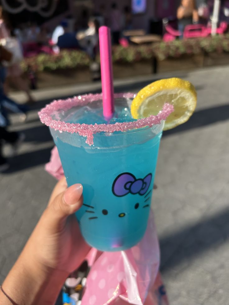 Hand holding blue drink in Hello Kitty cup with pink rim and lemon slice