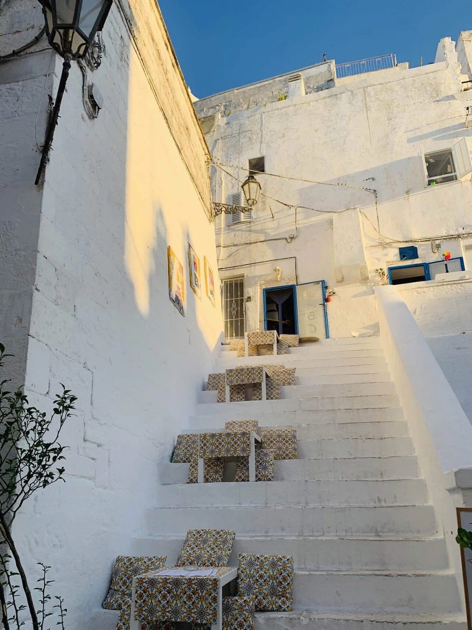 White stone steps between whitewashed walls in Ostuni, Italy with small cafe tables at the base