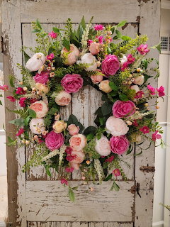 Colorful floral wreath with pink peonies and roses hanging on a rustic white wooden door