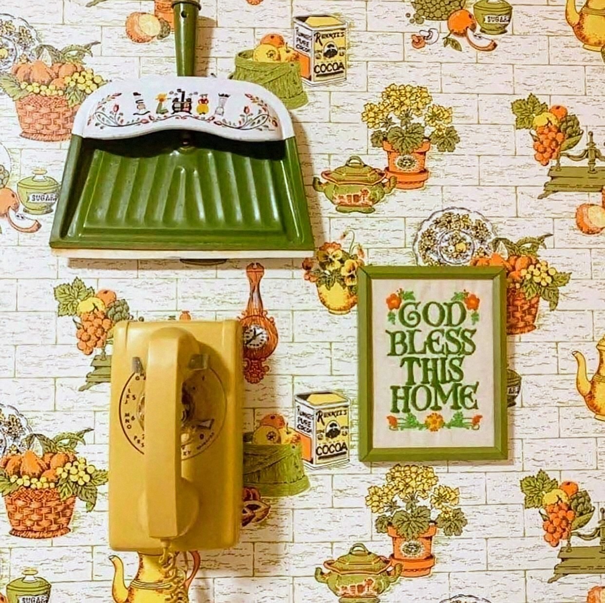 Vintage 1970s kitchen wall decor with a green appliance, yellow phone, framed sign, and floral wallpaper