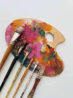 Wooden paint palette with rainbow colored paint splashes and several paintbrushes on white background
